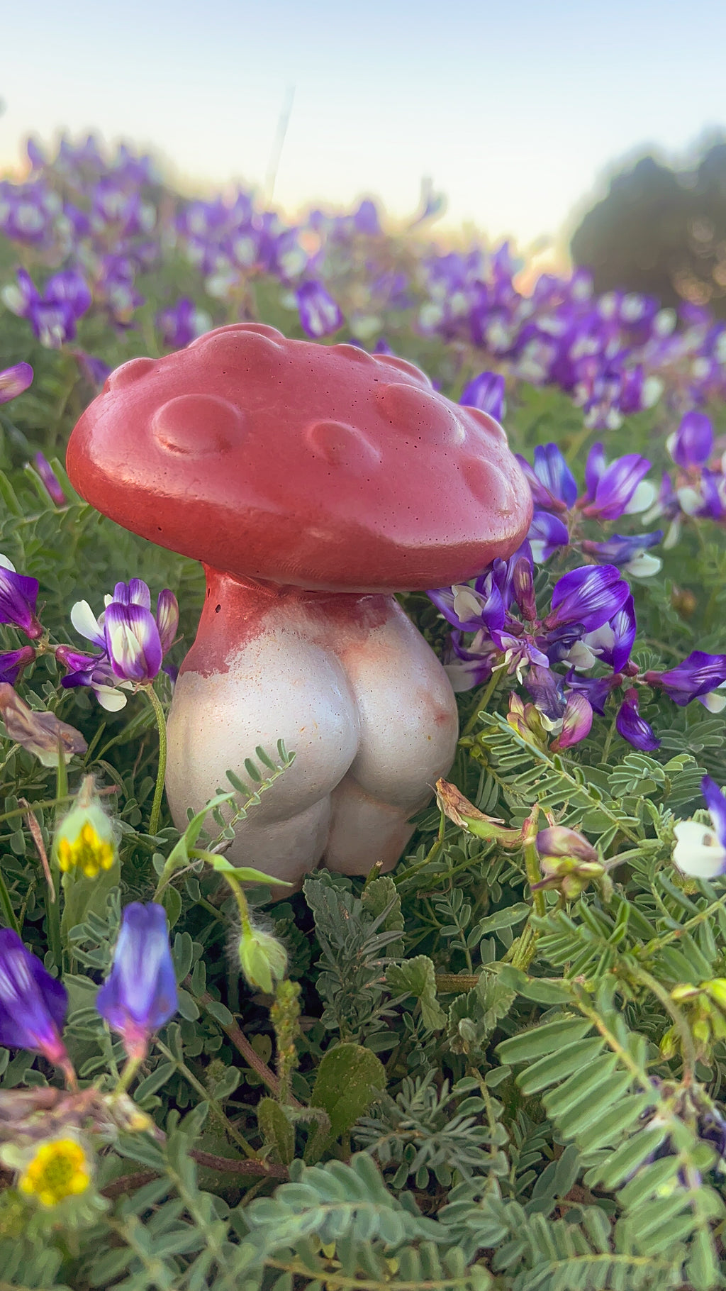 A hand-poured and dyed concrete garden stake designed to look like a red and white mushroom, placed in a bed of purple flowers.