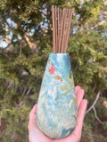 teal and orange vase with incense sticks in hole.